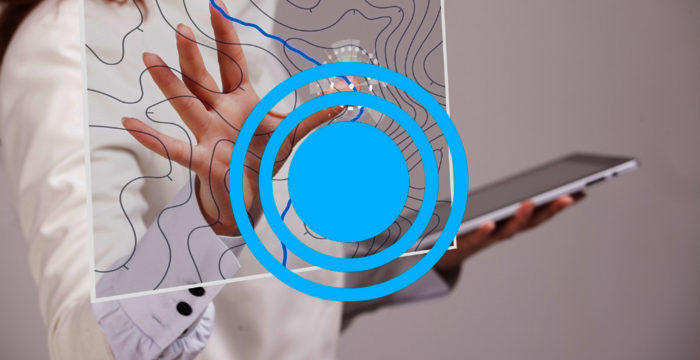 Eine Person bedient ein Tablet und interagiert mit einem transparenten Display, das eine topografische Kartenlinie zeigt; hervorstechend sind blaue konzentrische Kreise, die den Interaktionsbereich markieren.