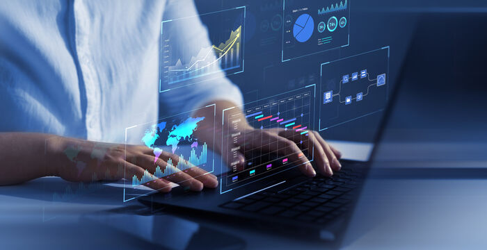 Eine Person tippt auf einem Laptop, während holografische Datenvisualisierungen – Diagramme, Grafiken und eine Weltkarte – über dem Bildschirm erscheinen.