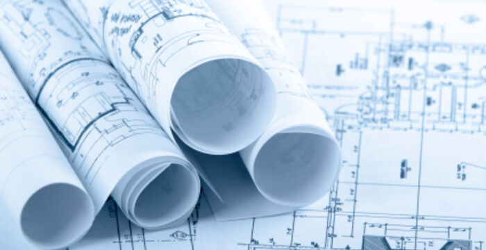 Mehrere eingerollte Architektenpläne liegen auf einem Tisch; blaue Drucke zeigen technische Zeichnungen und Grundrisse.