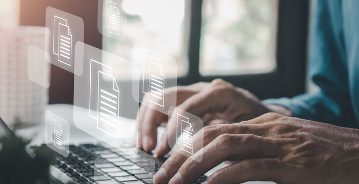 Eine Person tippt auf einem Laptop; über der Tastatur schweben transparente Dokumentensymbole, die digitale Dateien repräsentieren, während der Hintergrund unscharf bleibt.