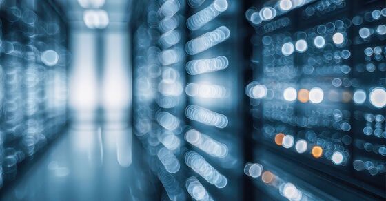Ein Serverraum mit zwei Reihen von Serverracks; der Gang zwischen ihnen führt zu einer hellen Tür im Hintergrund. Blau leuchtende LEDs erzeugen einen unscharfen Bokeh-Effekt und betonen die technologische Atmosphäre.
