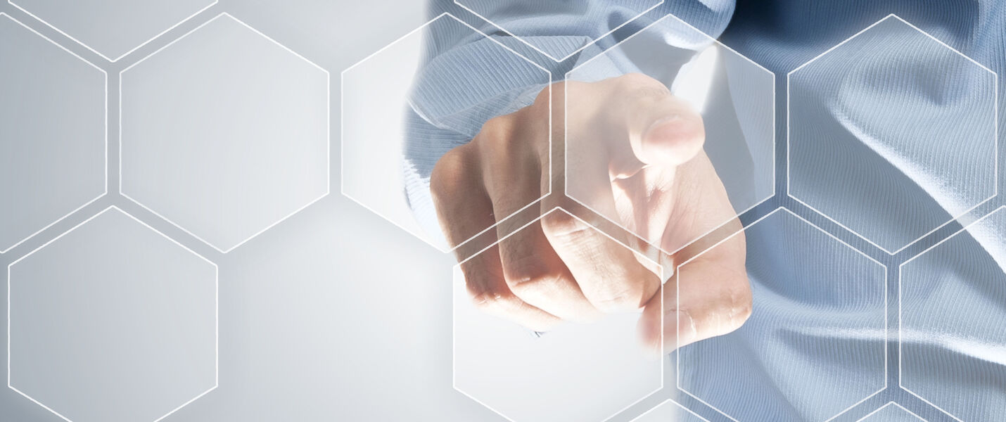 Eine Person in hellblauem Hemd zeigt mit dem Zeigefinger direkt auf den Betrachter; dahinter befindet sich ein abstraktes Muster aus weißen Hexagonlinien.