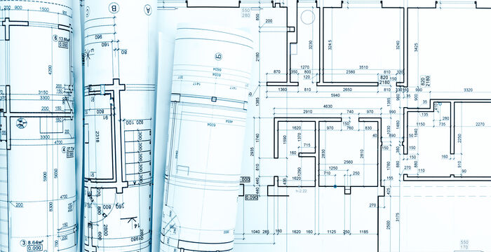 Mehrere Architekturpläne und Blaupausen liegen aus oder sind gerollt. Die technischen Zeichnungen zeigen Grundrisse, Maßlinien und Raumanordnungen mit vielen Linien, Maßen und Detailvermerken. Eine Bau- bzw. Planungs-Szene.
