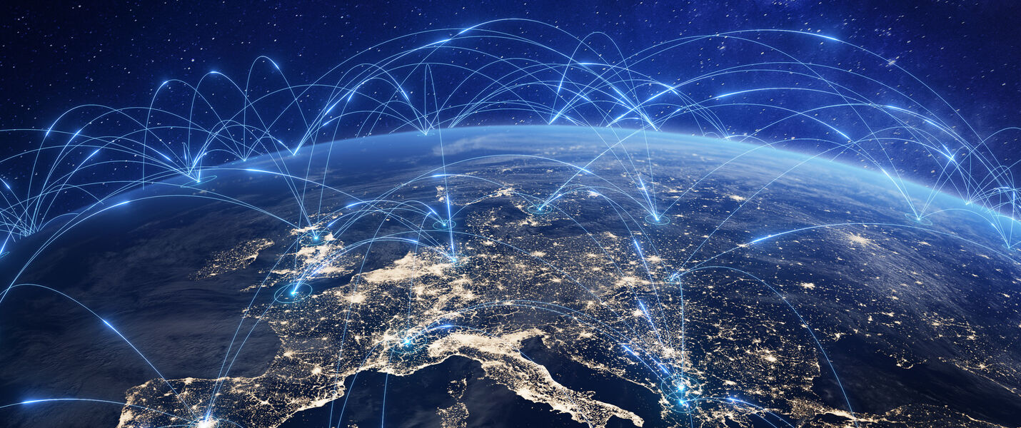 View of Earth from space at night, with illuminated continents and blue network lines arching across the globe, symbolizing global connectivity and digital communication networks.