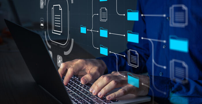 Person typing on a laptop with a holographic network of blue folders and documents connected by lines, illustrating digital file management and cloud storage.