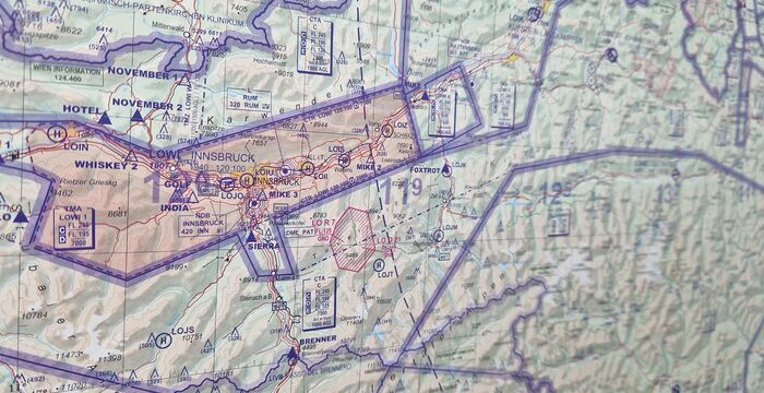 Eine topografische Karte mit einer violett markierten Route, Grenzlinien und Farbfeldern; zahlreiche Beschriftungen im NATO-Alphabet wie November, India, Hotel, Whiskey, Lima.