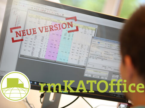Computerbildschirm zeigt eine tabellenartige Übersicht mit farblich markierten Feldern. Ein roter Stempel „NEUE VERSION“ liegt darüber. Unten links erscheinen das rmKATOffice-Logo und der Name der Software.